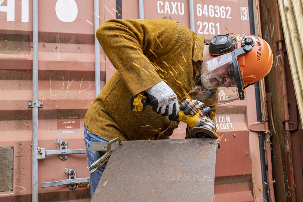 man wearing hard hat, earmuffs and face shield while grinding.