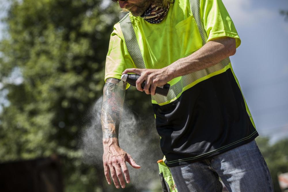 man spraying sunscreen on his arms.